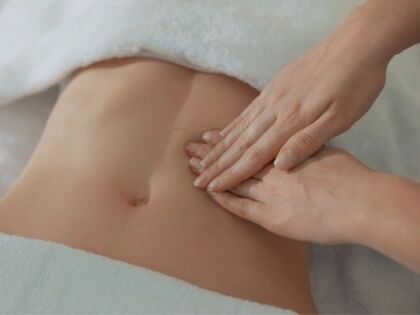 Hands giving a gentle stomach massage to a person lying on a towel